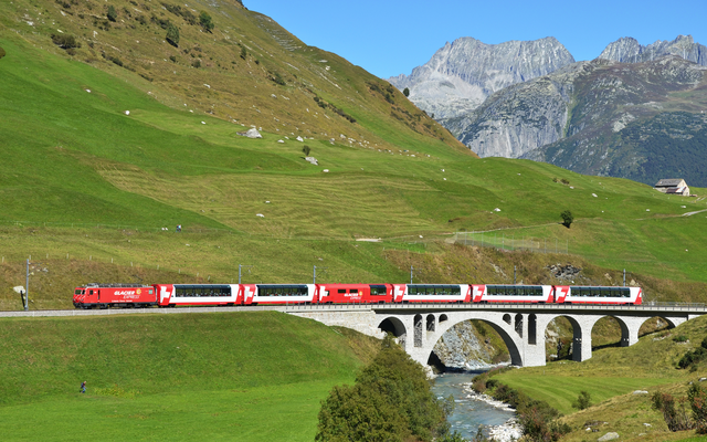 Roter Zug auf malerischer Brücke in Berglandschaft.