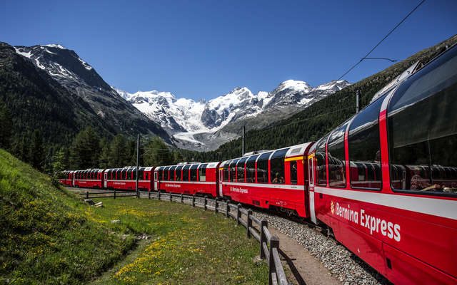 Roter Bernina Express in der Montebellokurve vor schneebedeckten Bergen und blauem Himmel.