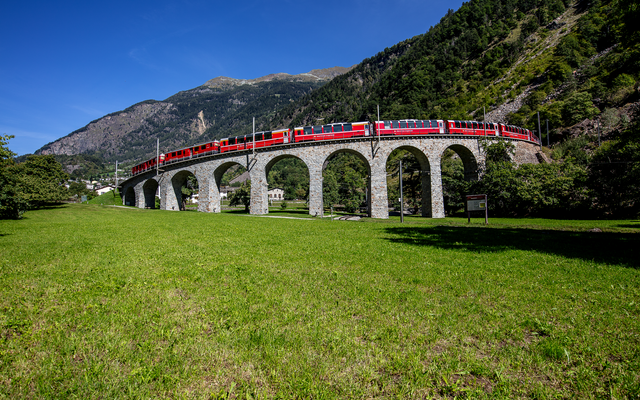Roter Zug des Bernina Express auf dem Kreisviadukt in Berglandschaft.