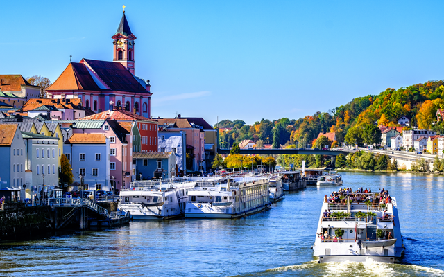 Bunte Gebäude und Boote an einem Fluss, Kirche im Hintergrund.