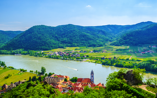 Blick auf ein Dorf mit Fluss und Bergen im Hintergrund.