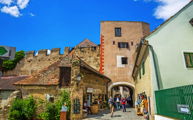 Eine malerische Altstadtgasse mit historischem Tor und Spaziergängern.