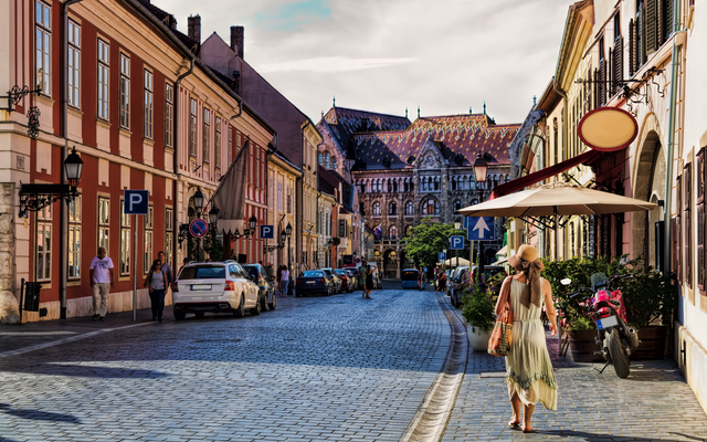 Straßenszene in einer Stadt mit historischen Gebäuden, Gehweg und Passanten.