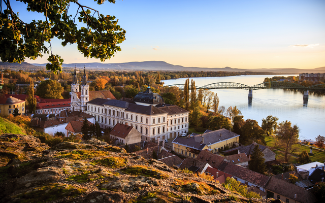 Flusslandschaft mit Brücke und historischem Gebäude bei Sonnenaufgang.