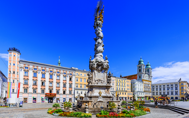 Barocke Dreifaltigkeitssäule auf einem Platz mit historischen Gebäuden im Hintergrund.