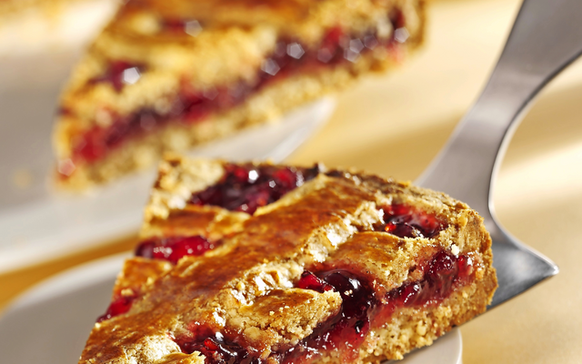 Ein Stück Linzertorte mit fruchtiger Füllung auf einer Tortenheber auf einem hellen Hintergrund.