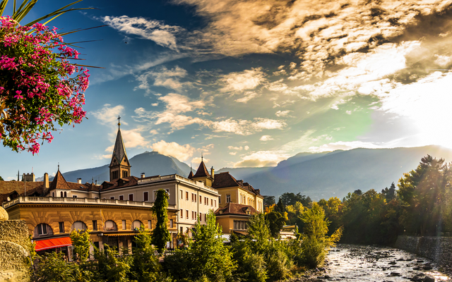 Stadtpanorama mit Fluss, Kirche und Bergen im Hintergrund bei Sonnenuntergang.