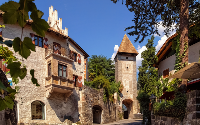 Mittelalterlicher Turm und historische Gebäude an sonniger Gasse.