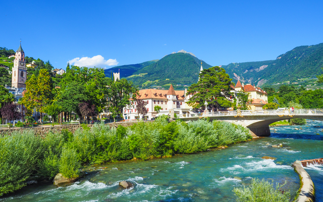 Fluss in einer Stadt mit Brücke und Bergen im Hintergrund bei klarem Himmel.