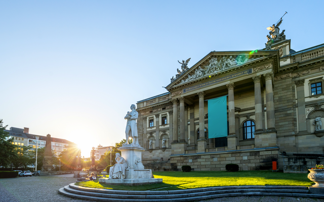 Historisches Gebäude mit Statue im Vordergrund bei Sonnenuntergang.