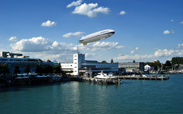 Ein Zeppelin fliegt über einem Hafen bei klarem Wetter.