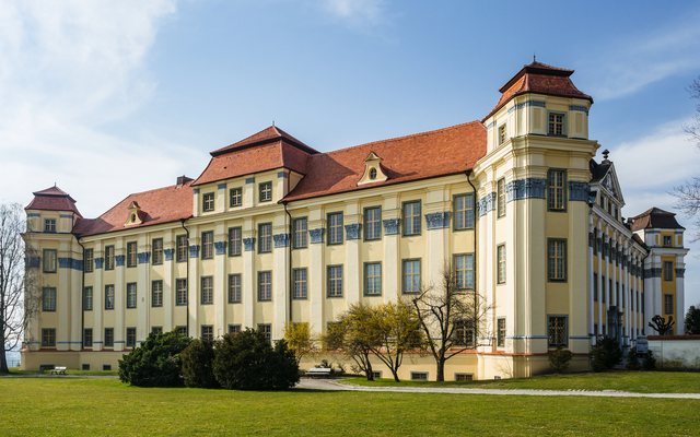 Großes, historisches Gebäude mit roten Dächern und gelber Fassade vor blauem Himmel.