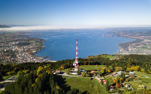 Luftaufnahme eines Sendemastes und Bodensee vor Alpenkulisse.