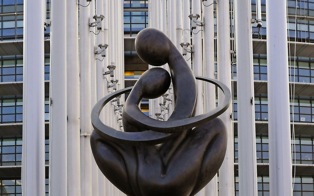 Moderne Skulptur vor einem Gebäude mit Säulen und Fenstern.