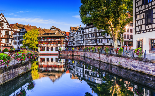 Fachwerkhäuser an einem Kanal in Straßburg, umgeben von bunten Blumen.
