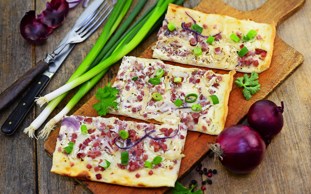 Flammkuchen mit Speck und Zwiebeln auf Holzbrett mit Frühlingszwiebeln.