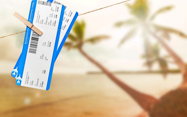 Zwei Flugtickets hängen mit Klammer vor unscharfem Strandhintergrund.