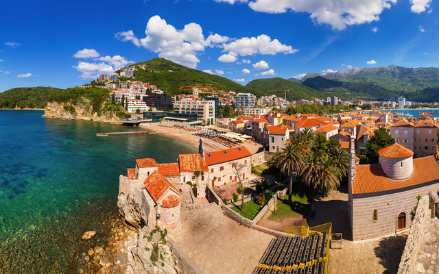 Panoramaansicht einer Küstenstadt mit Bergen und blauem Himmel im Hintergrund.