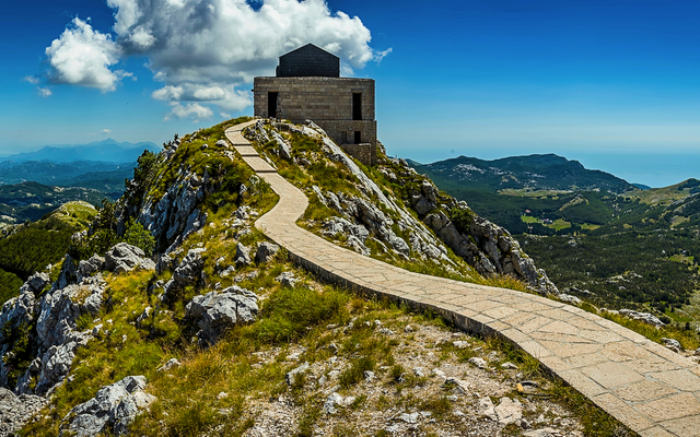Pfad zu einem Gebäude auf einem Berggipfel mit weitem Blick auf Landschaft und Himmel.