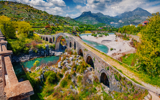 Steinbrücke über Fluss in grüner Berglandschaft bei Sonnenschein