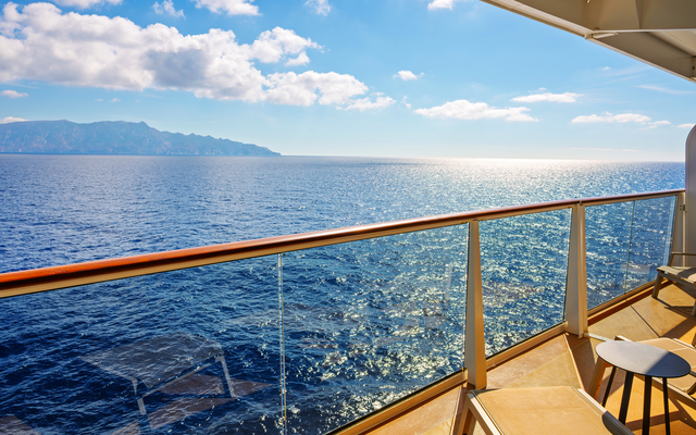 Blick von einem Kreuzfahrtschiff-Balkon auf das Meer und einen fernen Küstenstreifen.