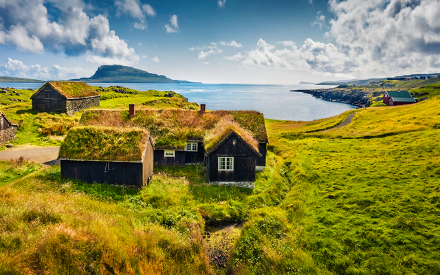 Grüne Wiesenlandschaft mit grasbewachsenen Häusern und Blick auf das Meer.