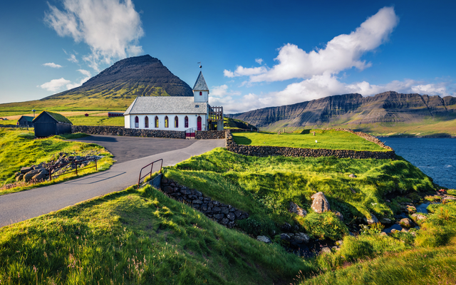 Kirche in grüner Landschaft mit Berg und blauem Himmel.