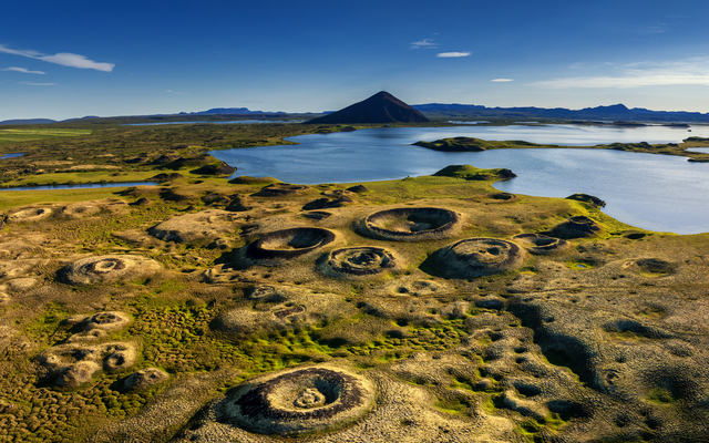 Vulkanische Landschaft mit Kratern und See im Hintergrund.