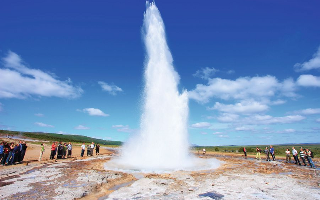 Geysir bricht aus, Menschen schauen zu, blauer Himmel, sonniger Tag.