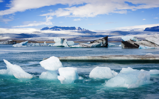 Eisberge treiben im klaren Wasser eines Gletschersees unter blauem Himmel.