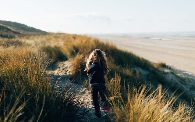 Kind geht einen grasbewachsenen Dünenpfad entlang in Richtung Strand.