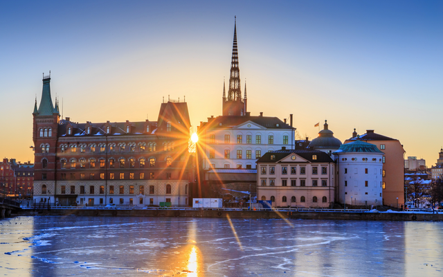 Sonnenuntergang hinter Gebäuden an einem gefrorenen Fluss.