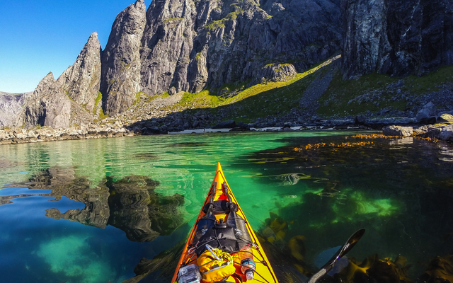 Person im Kajak auf türkisfarbenem Wasser in Refsvika, Lofoten, Norwegen.