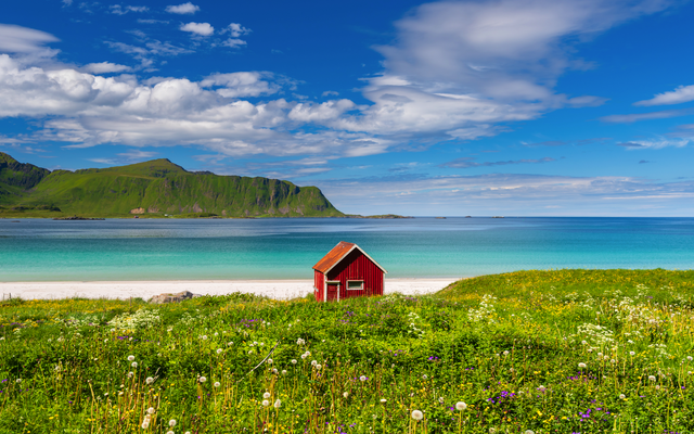 Rotes Haus an Küste mit grünem Hügel und blauem Himmel im Hintergrund