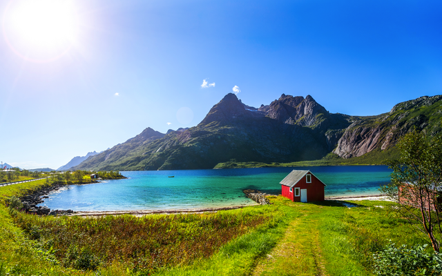 Rotes Haus am See mit Bergen und blauem Himmel im Hintergrund.