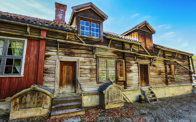 Altes Holzhaus mit roten Akzenten und Dachgauben bei klarem Himmel.