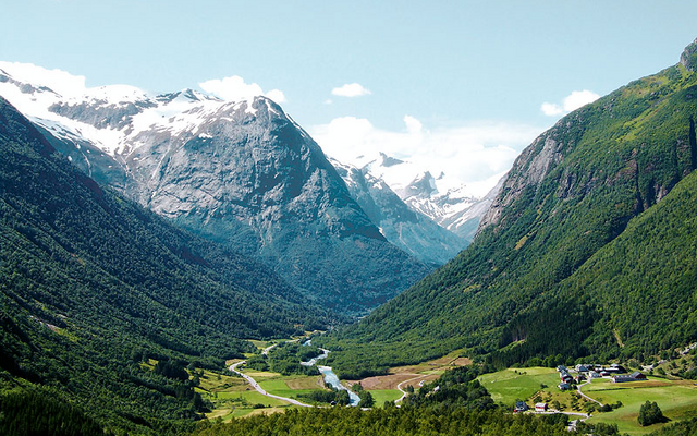 Blick auf eine grüne Gebirgslandschaft mit Fluss und schneebedeckten Gipfeln.