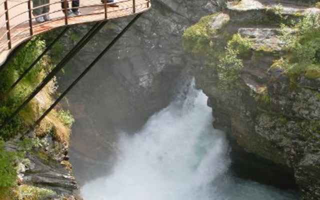 Personen auf einer Plattform betrachten eine tosende Schlucht in waldreicher Umgebung.