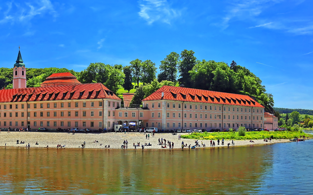 Panoramablick auf ein Gebäude am Flussufer mit Bäumen im Hintergrund.