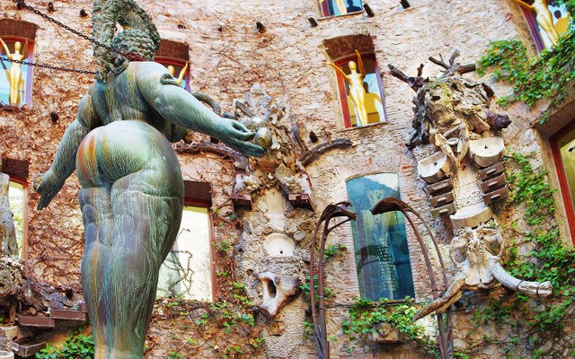Skulptur im Innenhof eines Museums, umgeben von Fenstern und Figuren an der Wand.