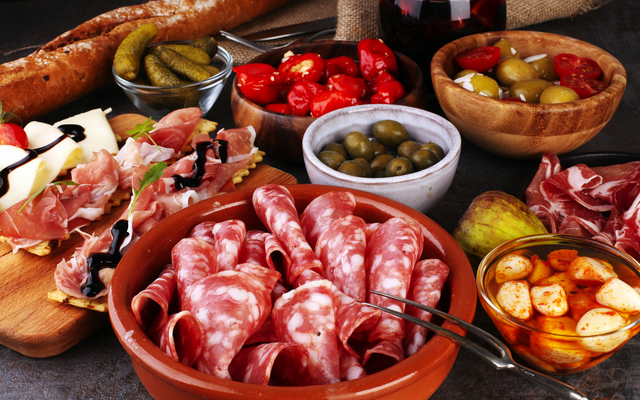 Verschiedene Antipasti auf Holzbrett mit Salami, Oliven, Brot und eingelegtem Gemüse.