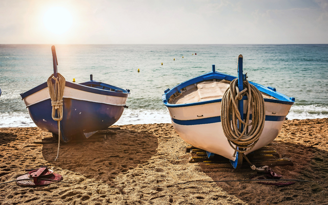 Zwei Boote am Sandstrand bei Sonnenuntergang am Meer.
