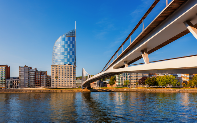Moderne Glasgebäude und elegante Brücke an einem Flussufer bei klarem Himmel.
