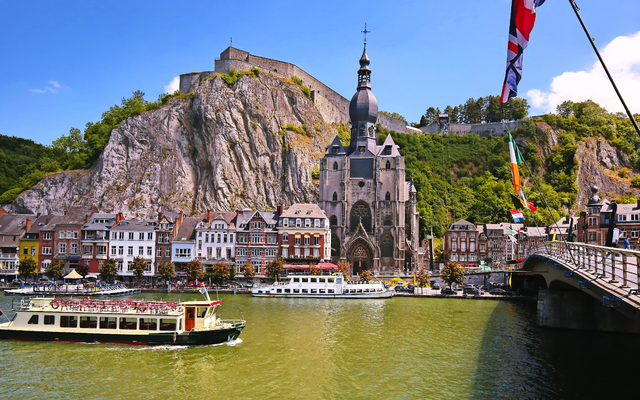 Stadtansicht von Dinant an der Maas mit Boot, Kirche und Felsen im Hintergrund.