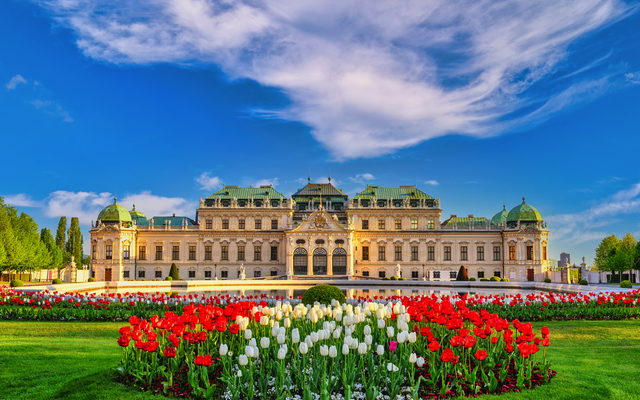 Barockes Schloss mit Blumenbeeten im Vordergrund und blauem Himmel.