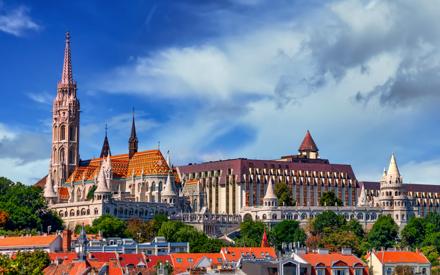 Kirche mit Türmen und geschichtsträchtigen Gebäuden im neogotischen Stil vor blauem Himmel.