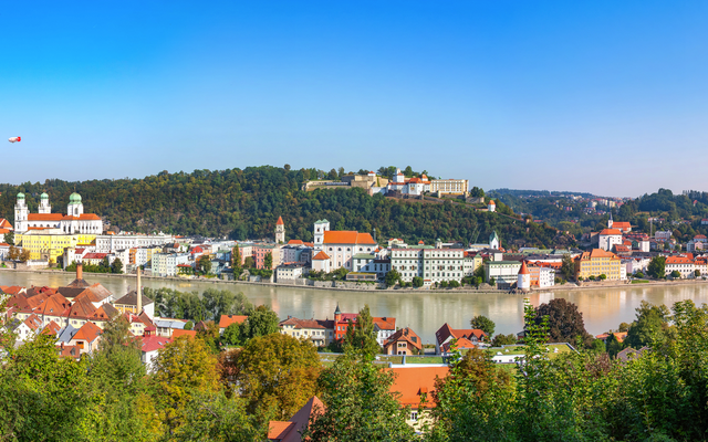 Panoramablick auf eine Stadt mit Fluss und bewaldeten Hügeln.