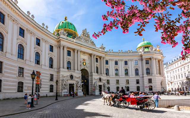Hofburg Wien im Frühling mit Pferdekutsche und blühenden Bäumen.