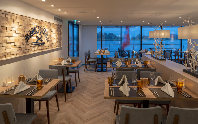 Innenansicht eines stilvollen Restaurants mit gedeckten Tischen und einem großen Logo an der Wand.