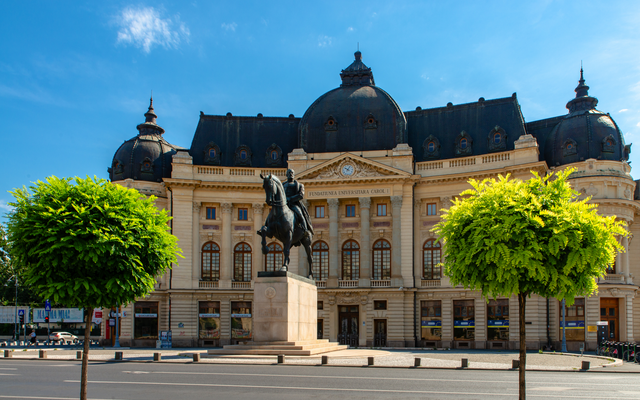 Historisches Gebäude mit Reiterstatue und zwei Bäumen im Vordergrund.